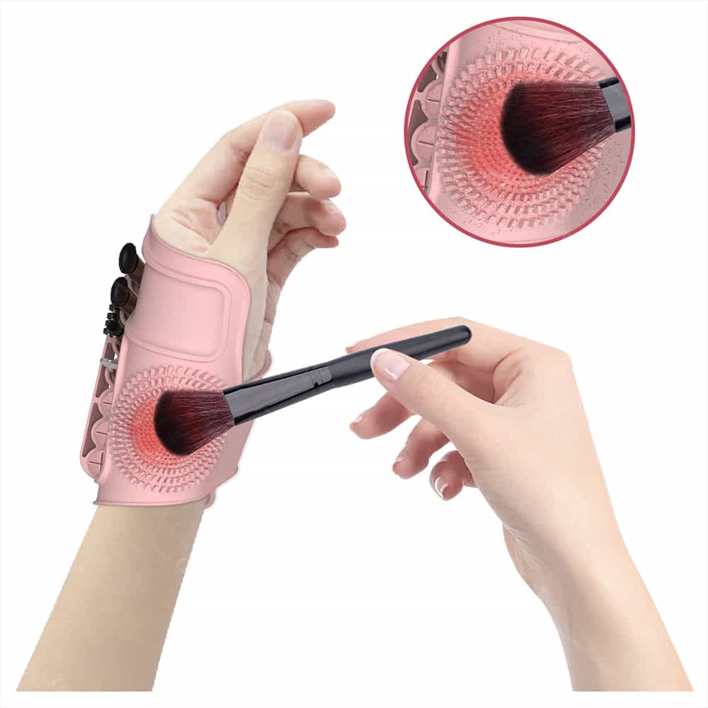 Pink silicone wrist palette for holding makeup brushes, featuring textured cleaning pad and adjustable strap.